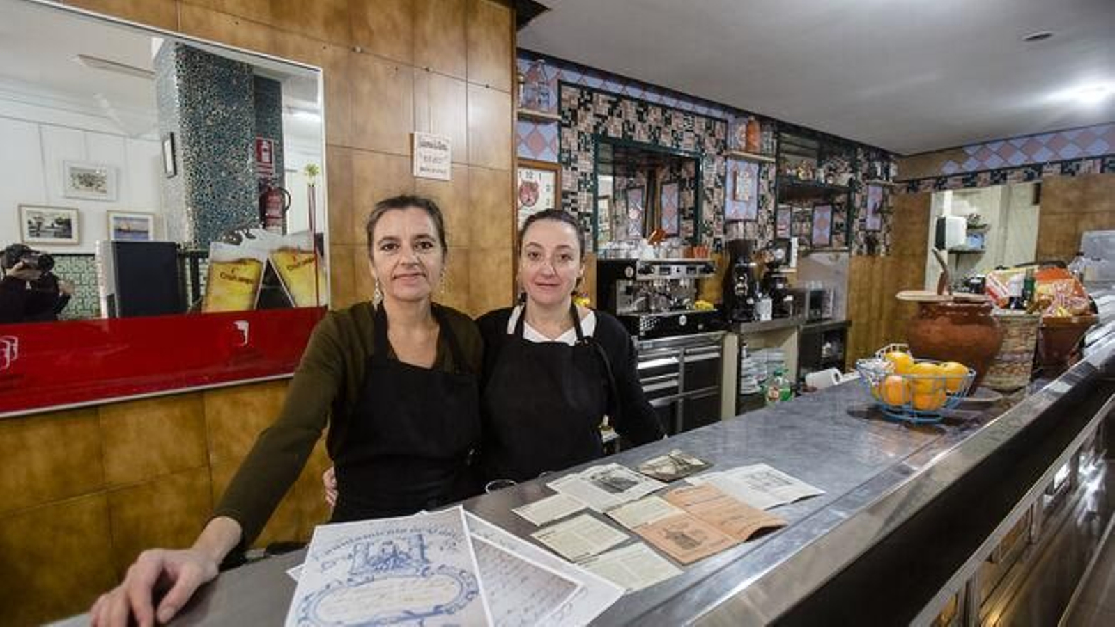 Natalia y Cristina tras la barra con los recortes de prensa y archivos históricos sobre el local