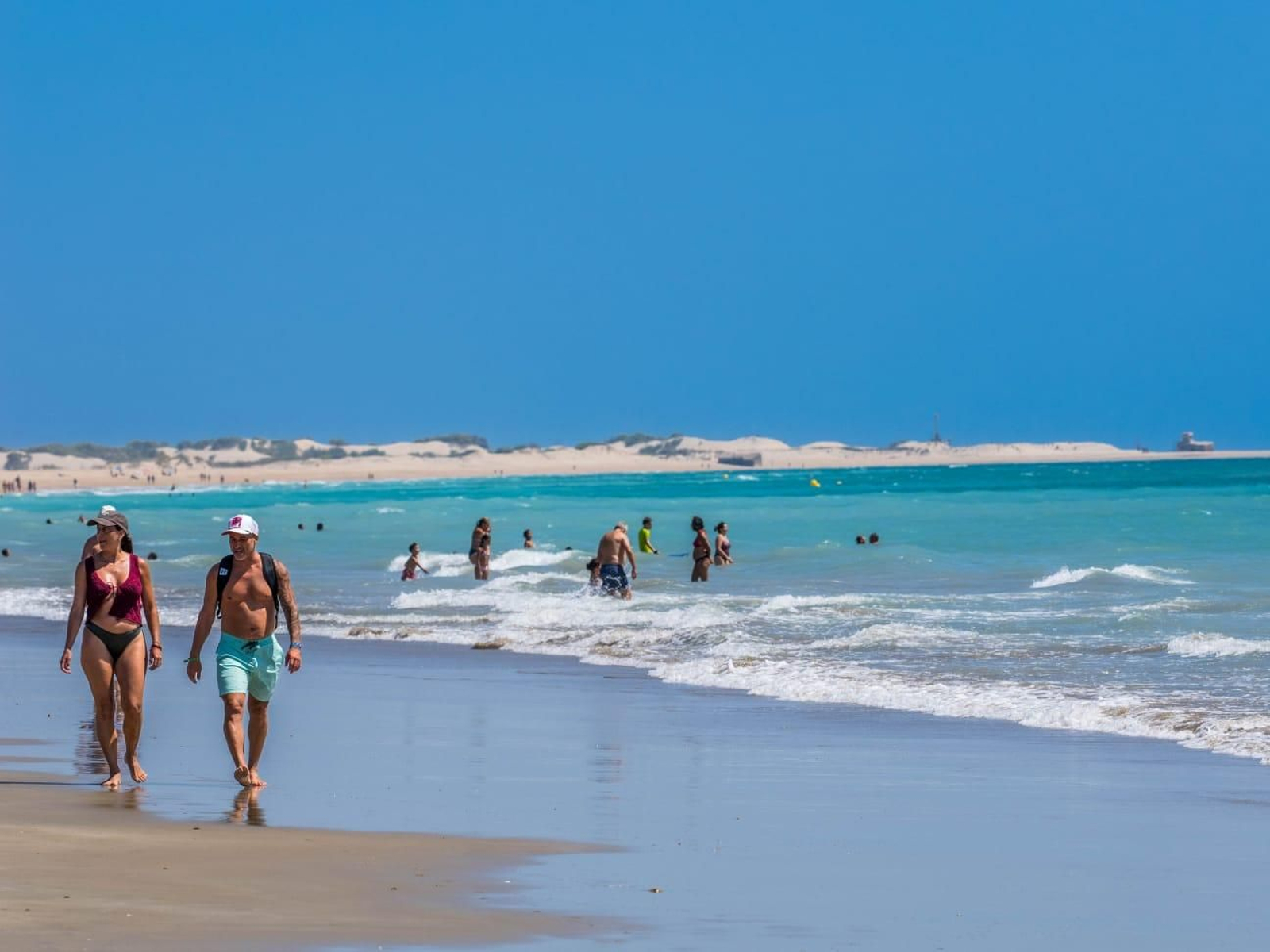 Varios bañistas pasean por la orilla de la playa isleña.