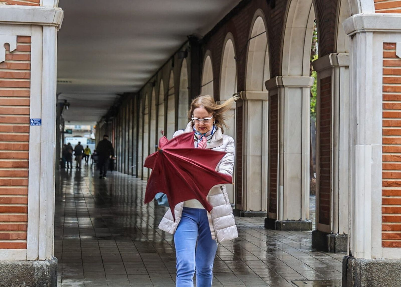 Una mujer trata de abrir su paraguas en un día de mucho viento en Huelva.