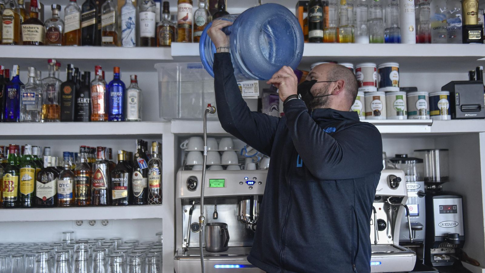 El propietario de una cafetería llena con agua de una garrafa la cafetera, ante la prohibición de usar la del grifo.