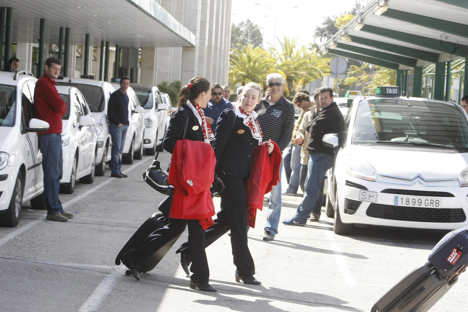 Dos azafatas pasan por delante de las paradas donde los taxistas esperan a los pasajeros del aeropuerto de Jerez.