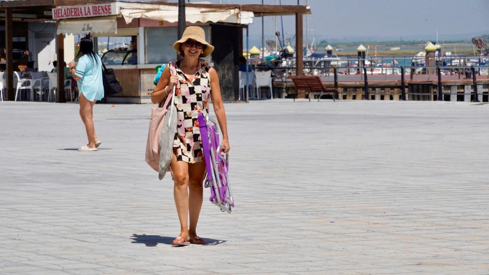 Una mujer lleva varias bolsas y una silla para pasar el día en la playa.