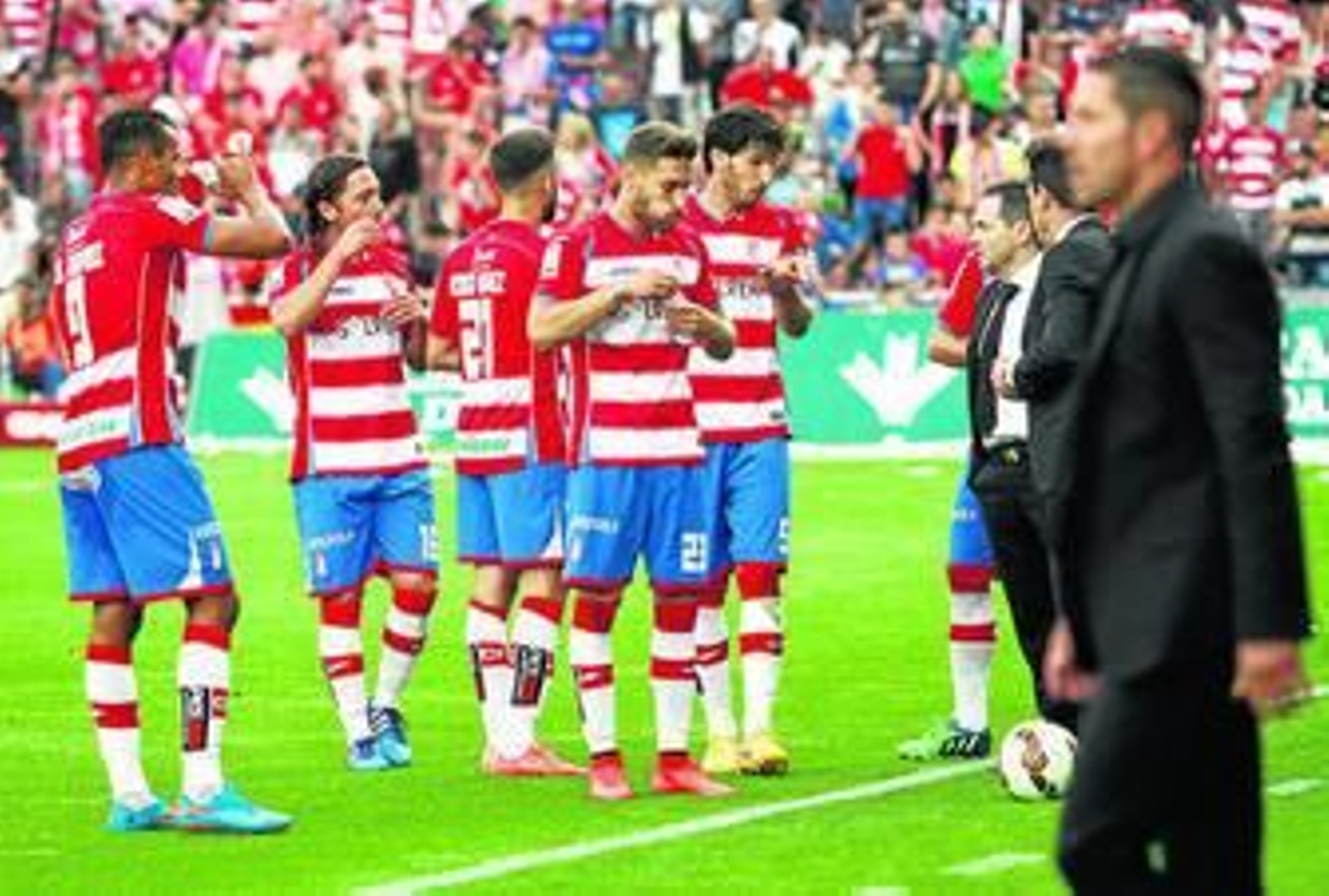 Varios jugadores del Granada se refrescan, con Simeone observando a los suyos en primer plano.