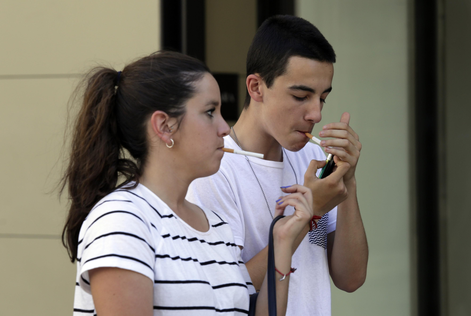 Dos jóvenes encienden un cigarrillo.
