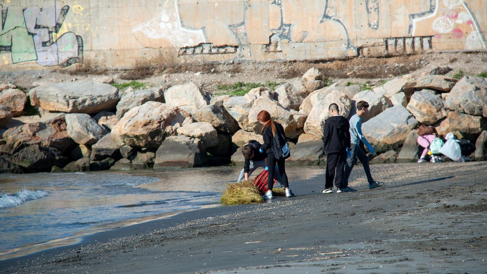 Varios alumnos intentan retirar una caja de plástico incrustrada en la arena