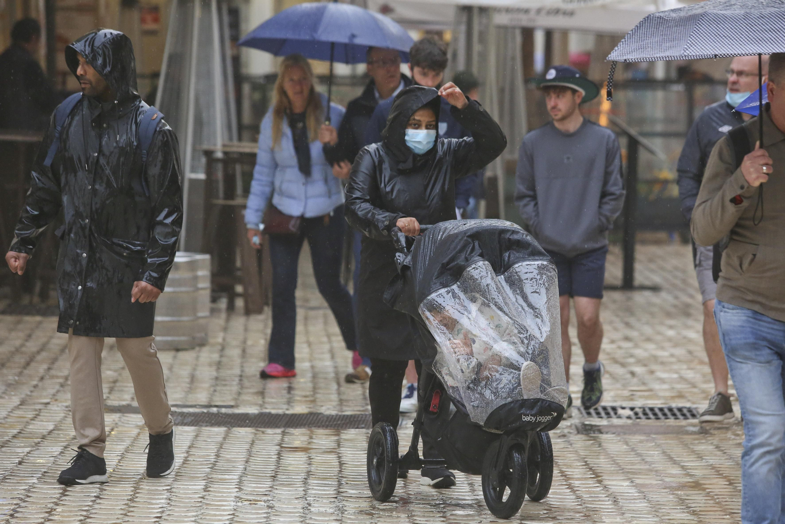 Varias personas se protegen de la lluvia en Málaga con chubasqueros y paraguas. Varias personas se protegen de la lluvia en Málaga con chubasqueros y paraguas.
