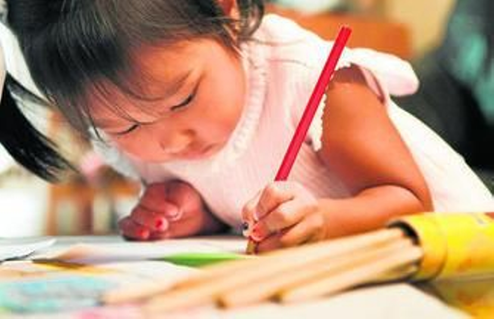 1. Una niña pequeña de origen asiático dibuja en un papel con un lápiz rojo.  2. Las familias deben enfrentarse a unos retos o tareas propias de la adopción como el desarrollo de lazos afectivos.