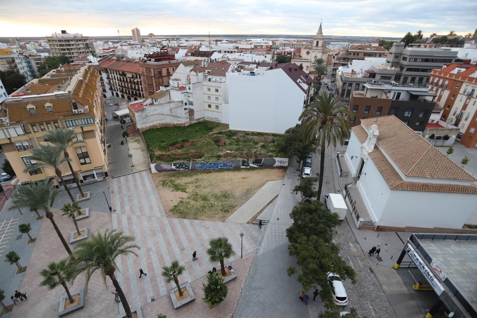Aspecto general de la plaza en la que se ve cómo no está terminada y el solar que lleva dos décadas con un muro.