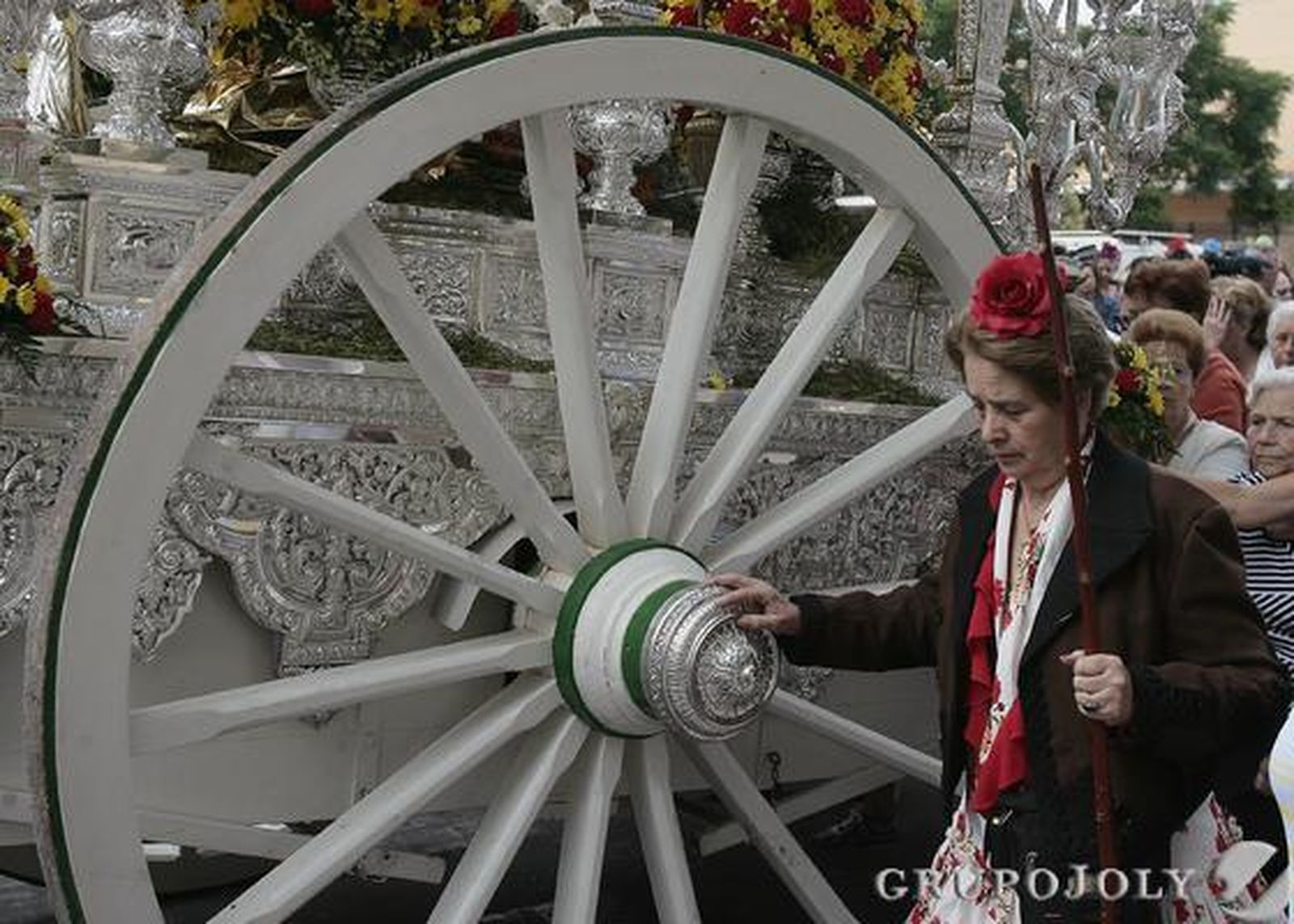 Una hermana, ataviada de rociera, camina junto a la gran rueda del carruaje del simpecado.

Foto: José Ángel García