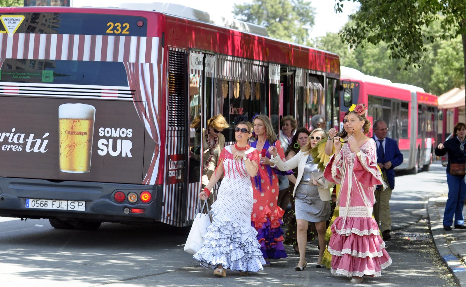 Mujeres vestidas de flamenca bajan de un autobús de Tussam en las proximidades a la Feria.
