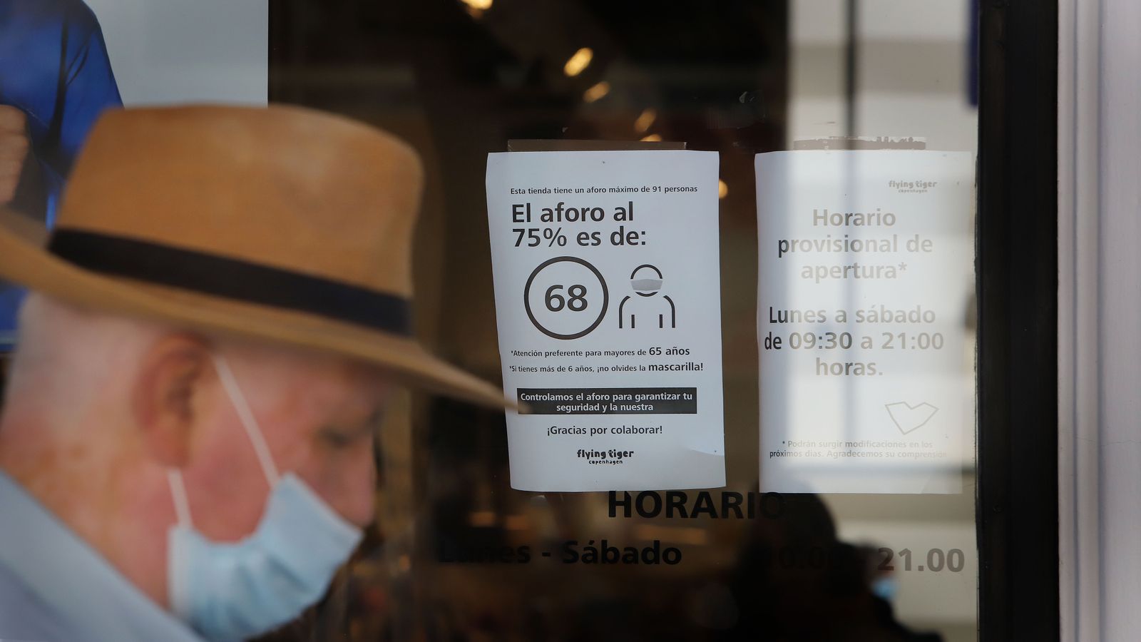 Un señor con la mascarilla puesta pasa por un establecimiento donde se indican las medidas de seguridad.