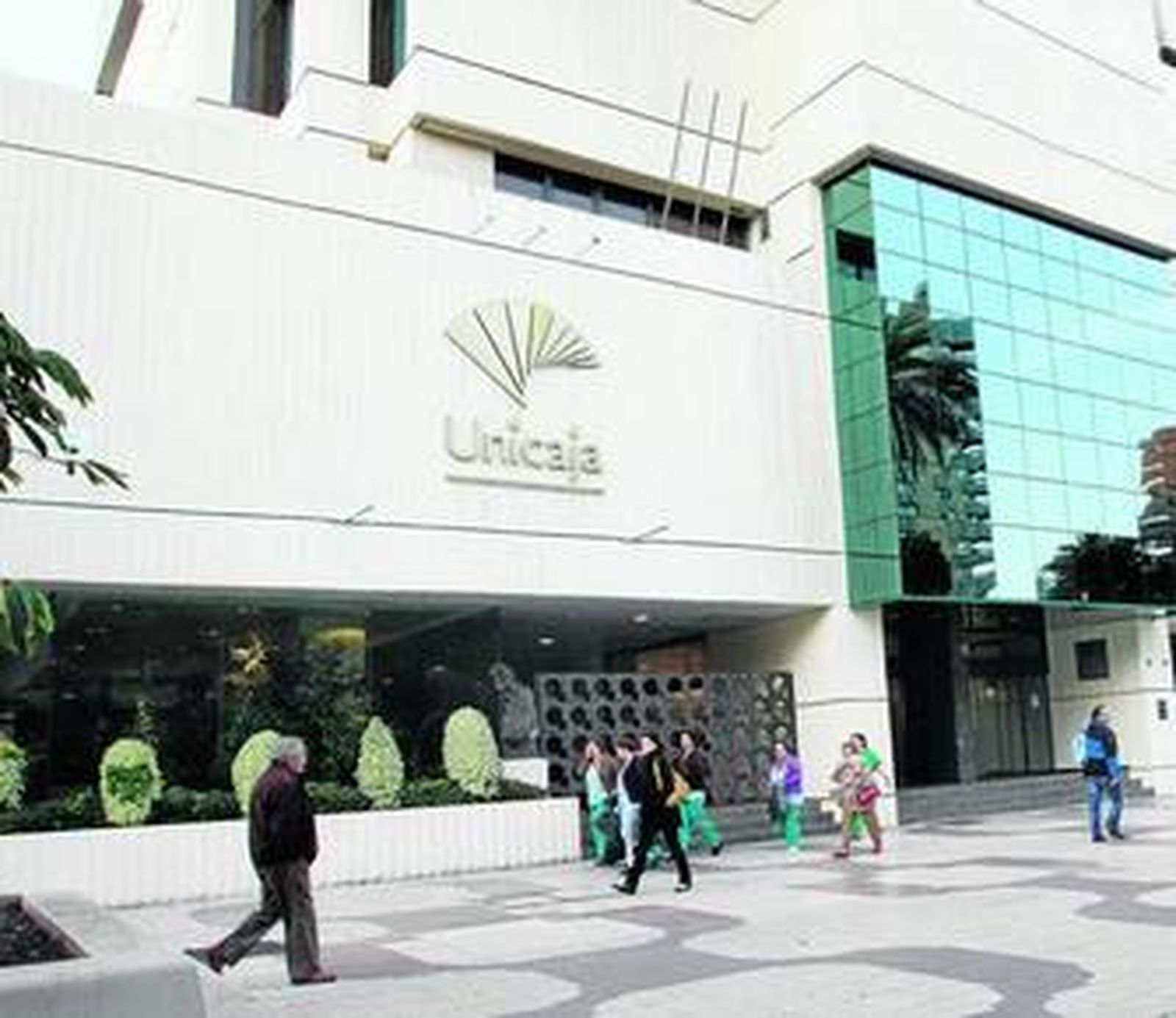 Varias personas pasan por delante de la sede central de Unicaja en Málaga.