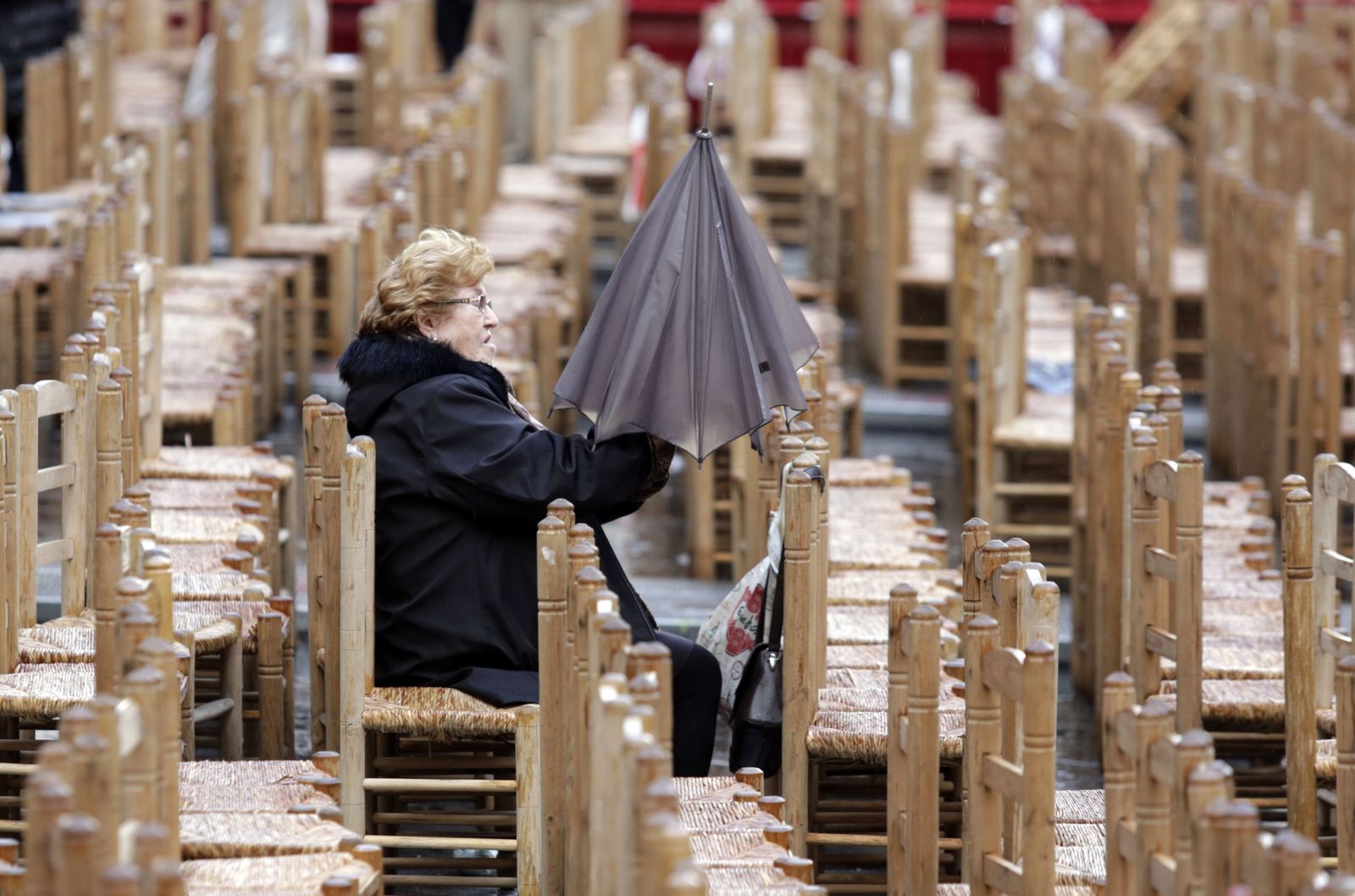Una mujer cierra su paraguas en las sillas de la carrera oficial.