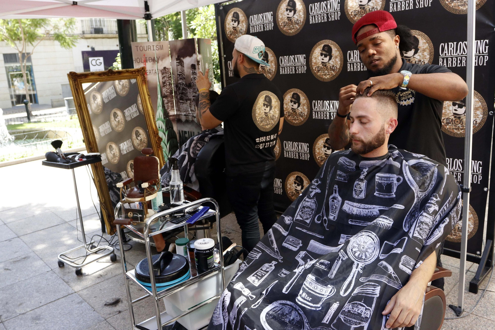 Carlos King junto a uno de sus empleados en plena faena de corte de pelo al aire libre en la Plaza del Educador.