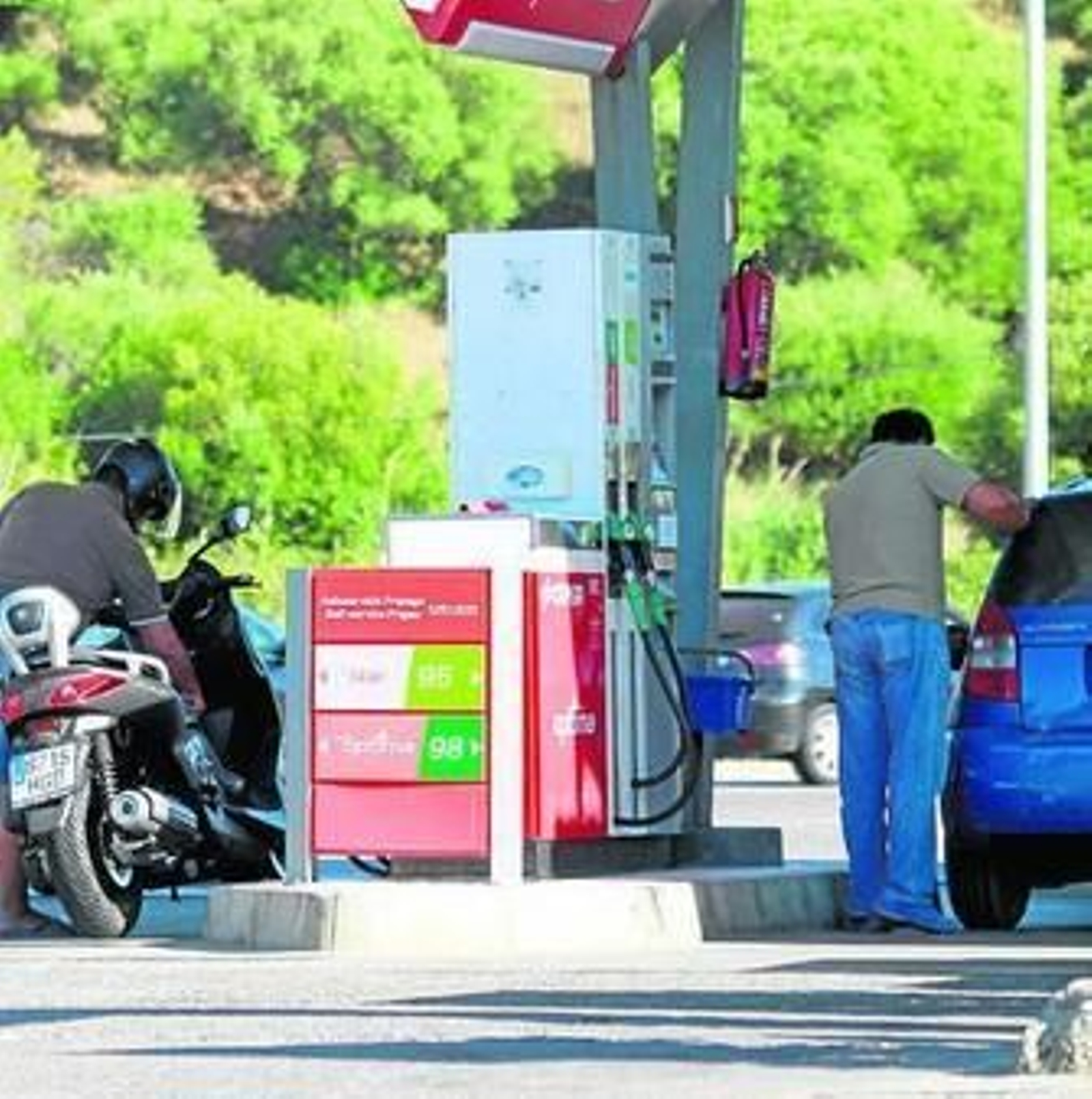 Varias personas repostan en una gasolinera. Varias personas repostan en una gasolinera.