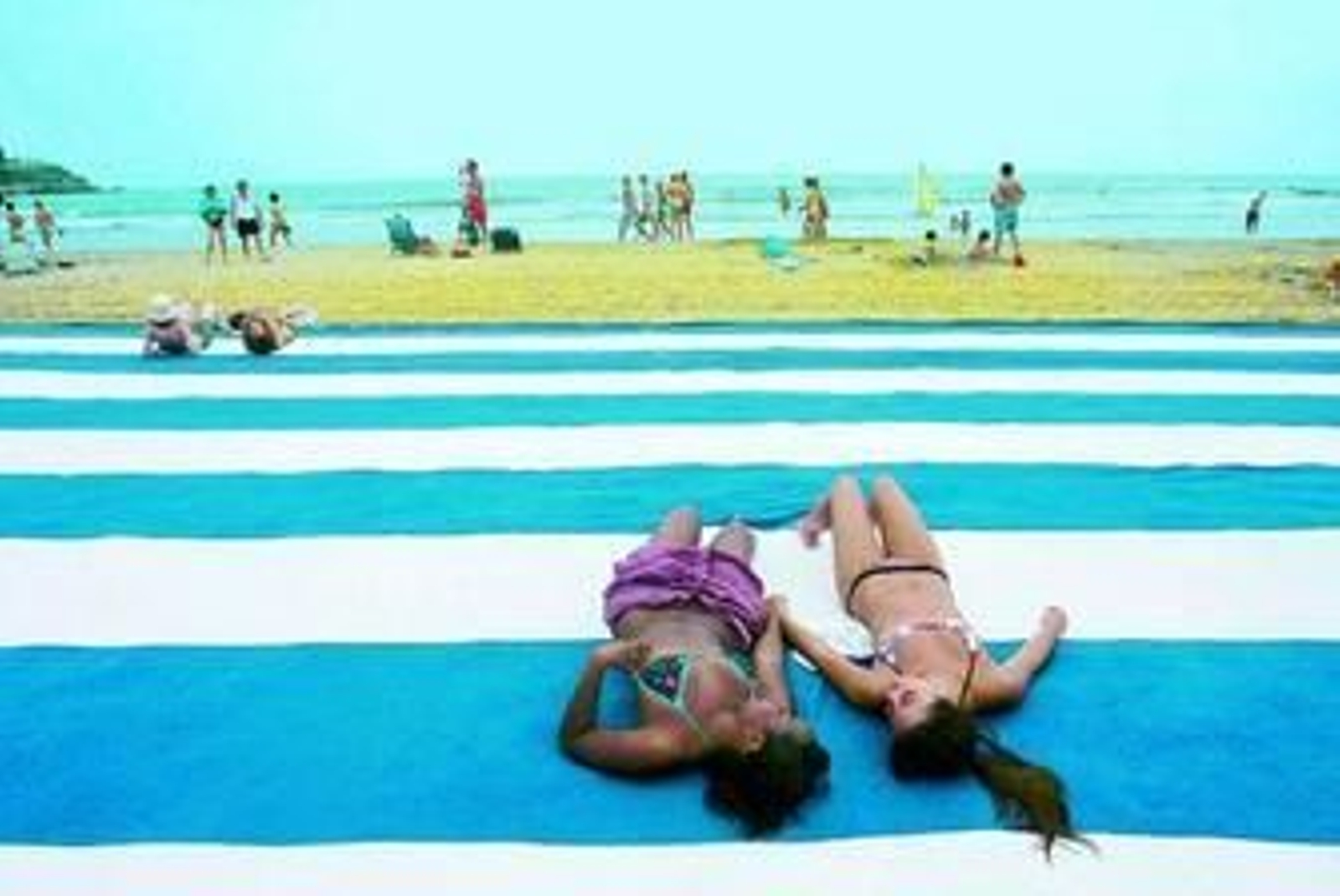 Dos jóvenes descansan en una toalla gigante del colectivo OTU OYO en la playa del Voramar.