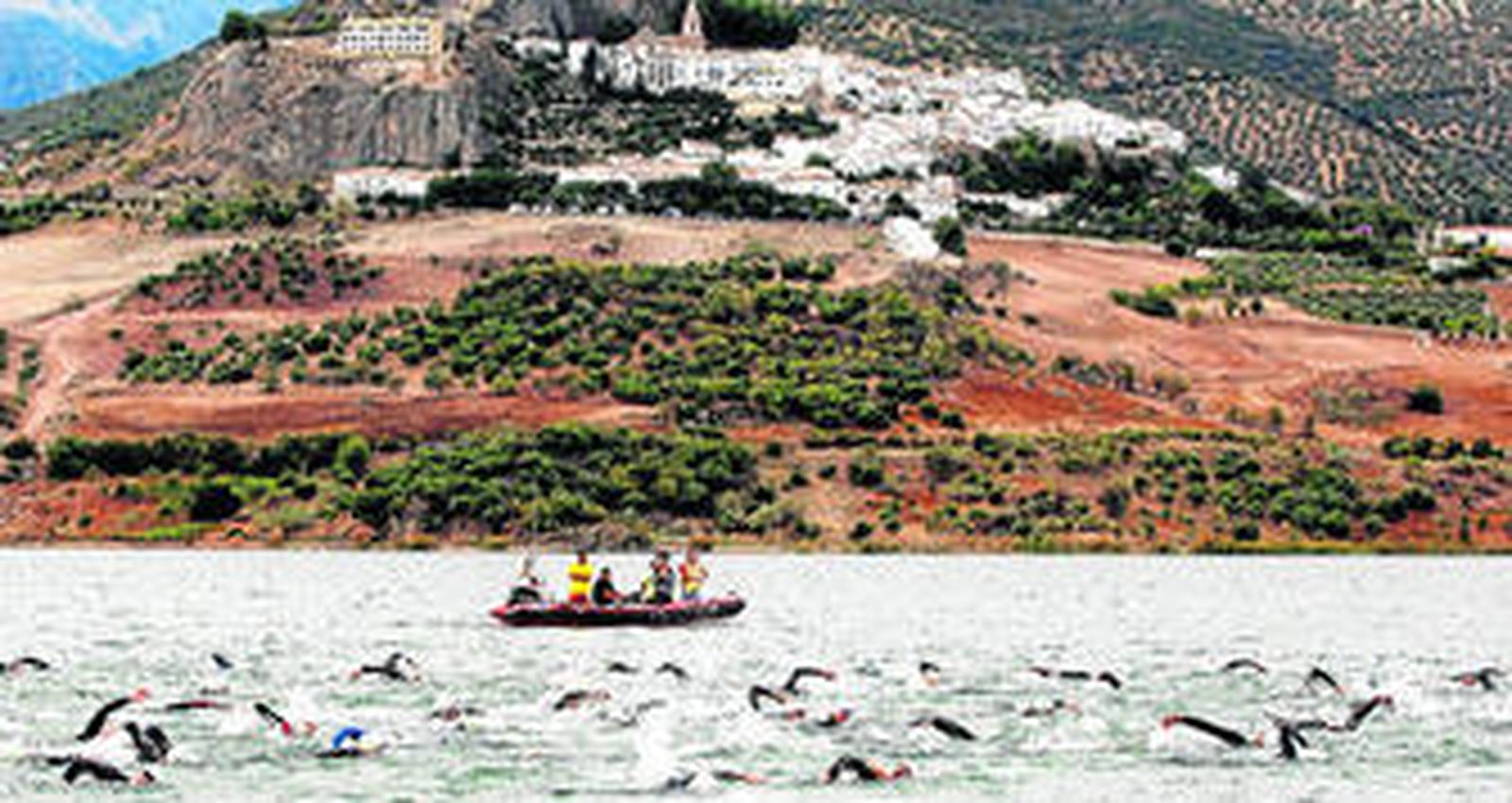 Los participantes durante la fase inicial de natación en el embalse de Zahara de la Sierra, con la localidad al fondo.