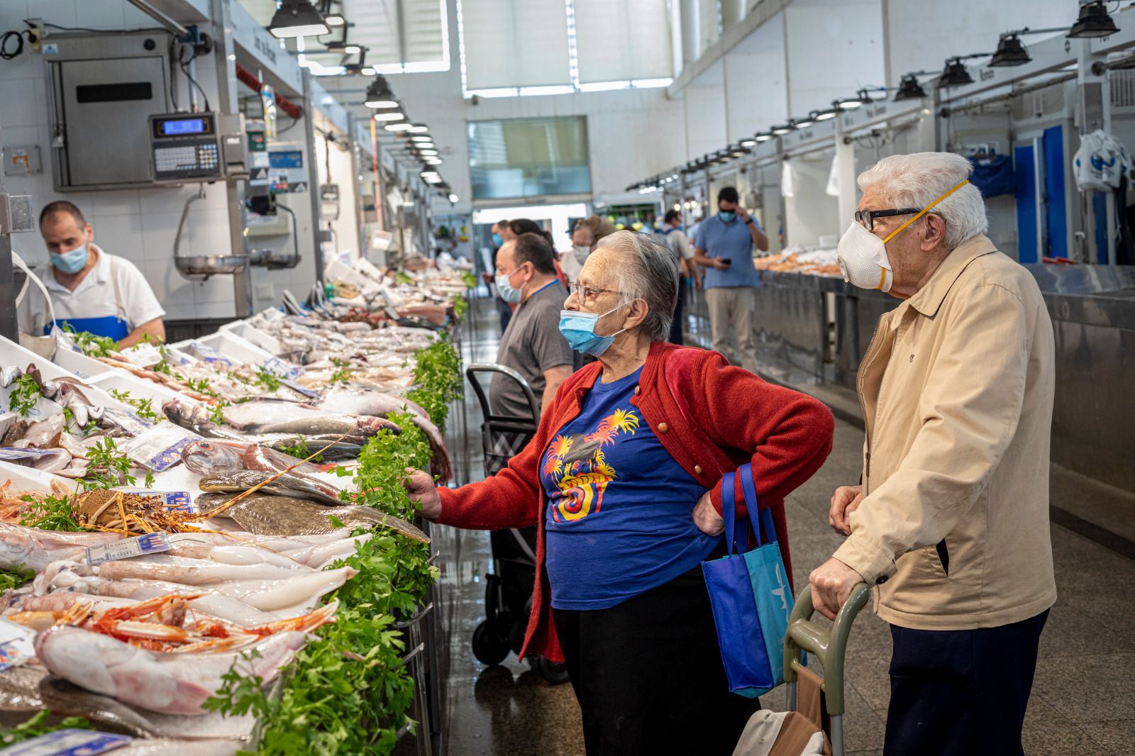 Un par de personas mayores compran pescado en el Mercado Central con sus mascarillas.