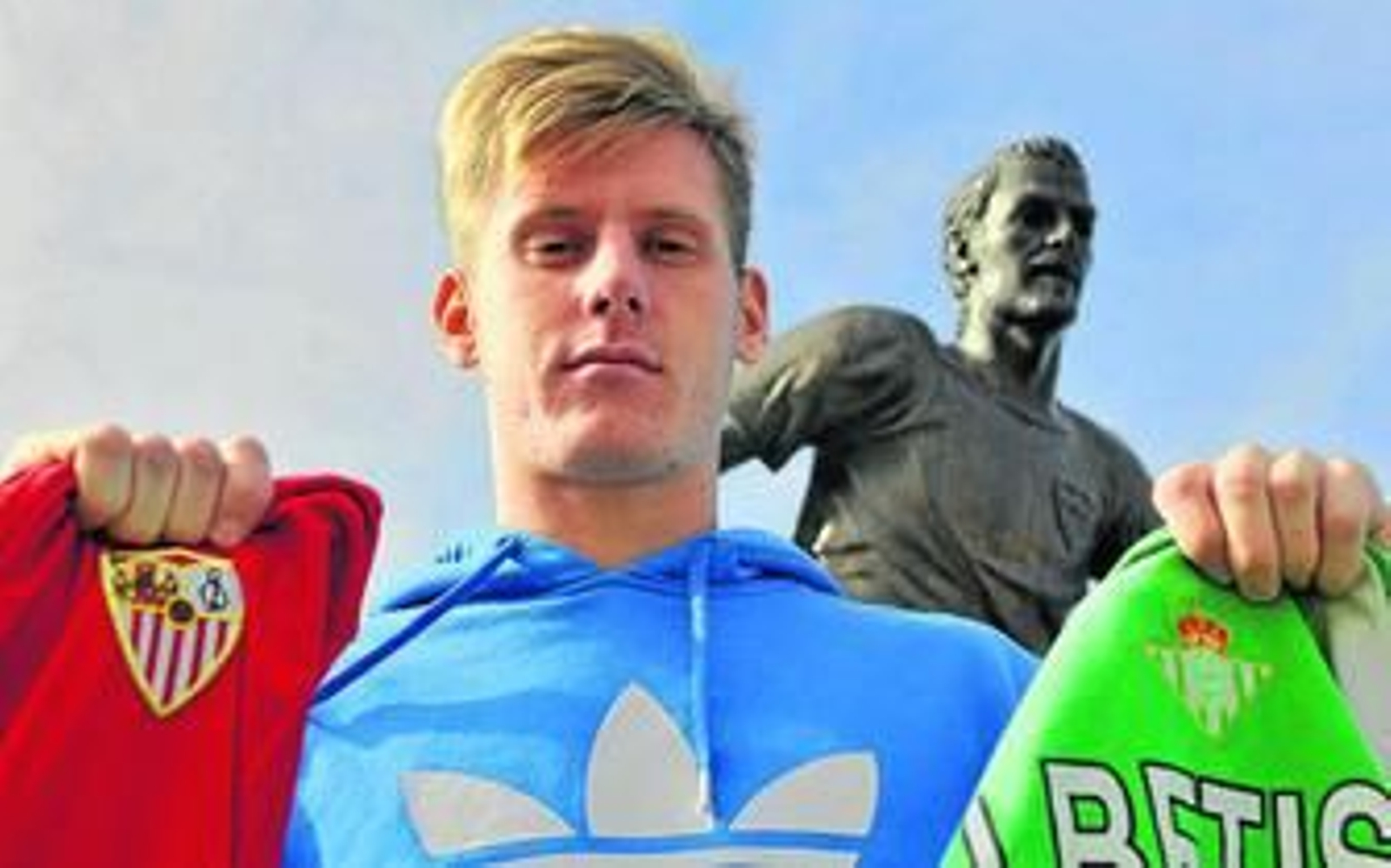 Adrian Wojcik, delante del monumento a Puerta, muestra las dos camisetas que ha lucido desde que llegó a Sevilla.