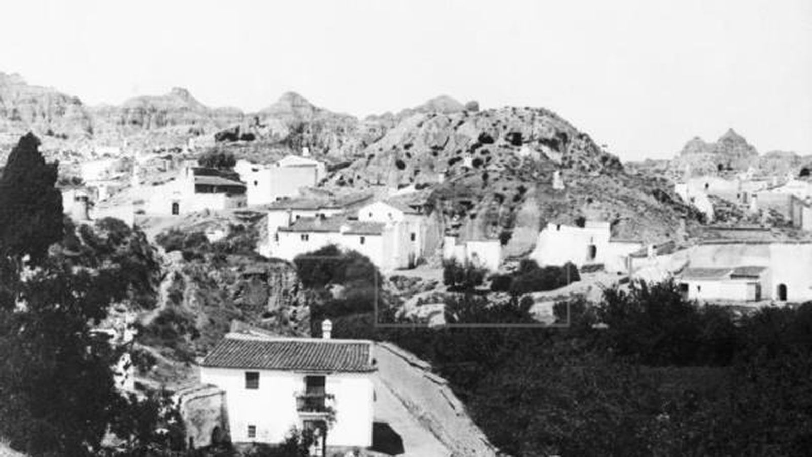 Fotografía del primer tercio del siglo XX de unas cuevas con Sierra Nevada al fondo.