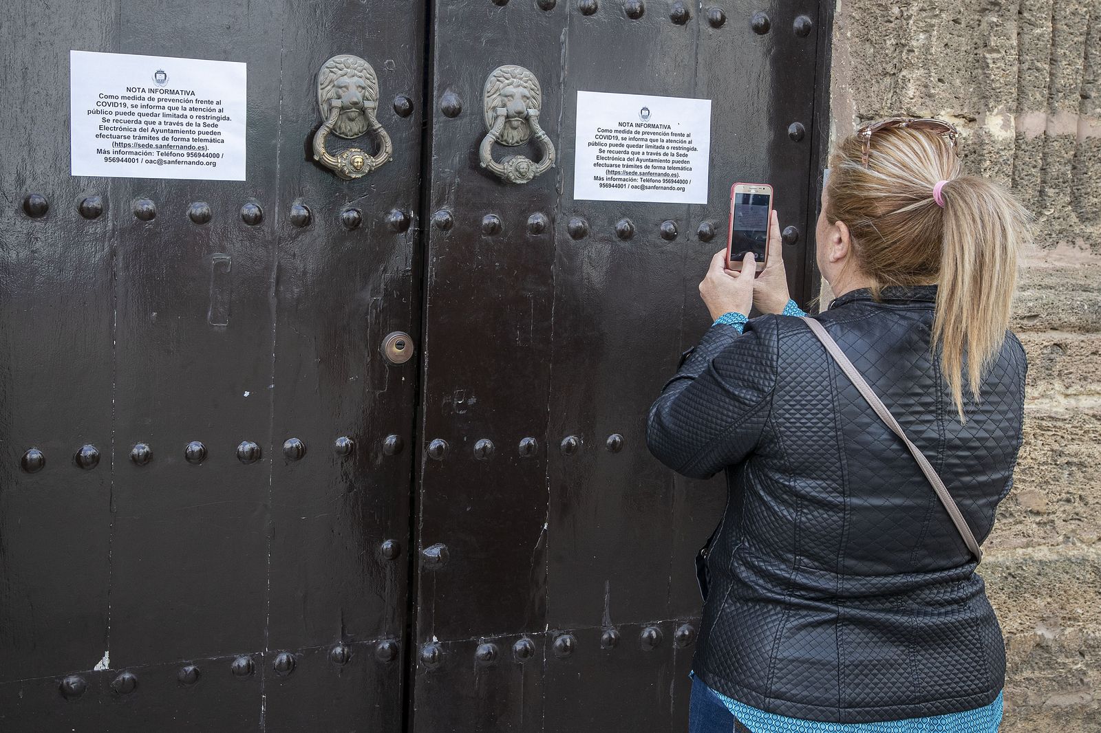 Una mujer toma una fotografía del cartel que avisa de las restricciones de atención presencial en la sede de Alcaldía.