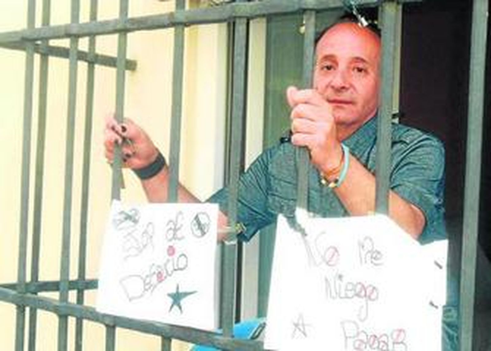 José Luis González, inquilino de la vivienda, muestra carteles desde el interior de la misma.
