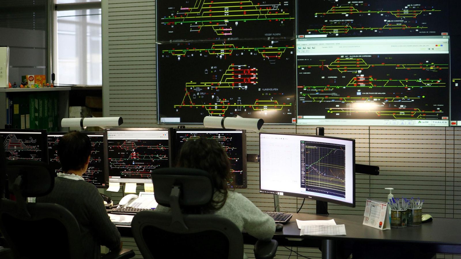 Dos técnicos, ante sus monitores y el 'videowall' que recoge las líneas que controla el CRC de Córdoba.