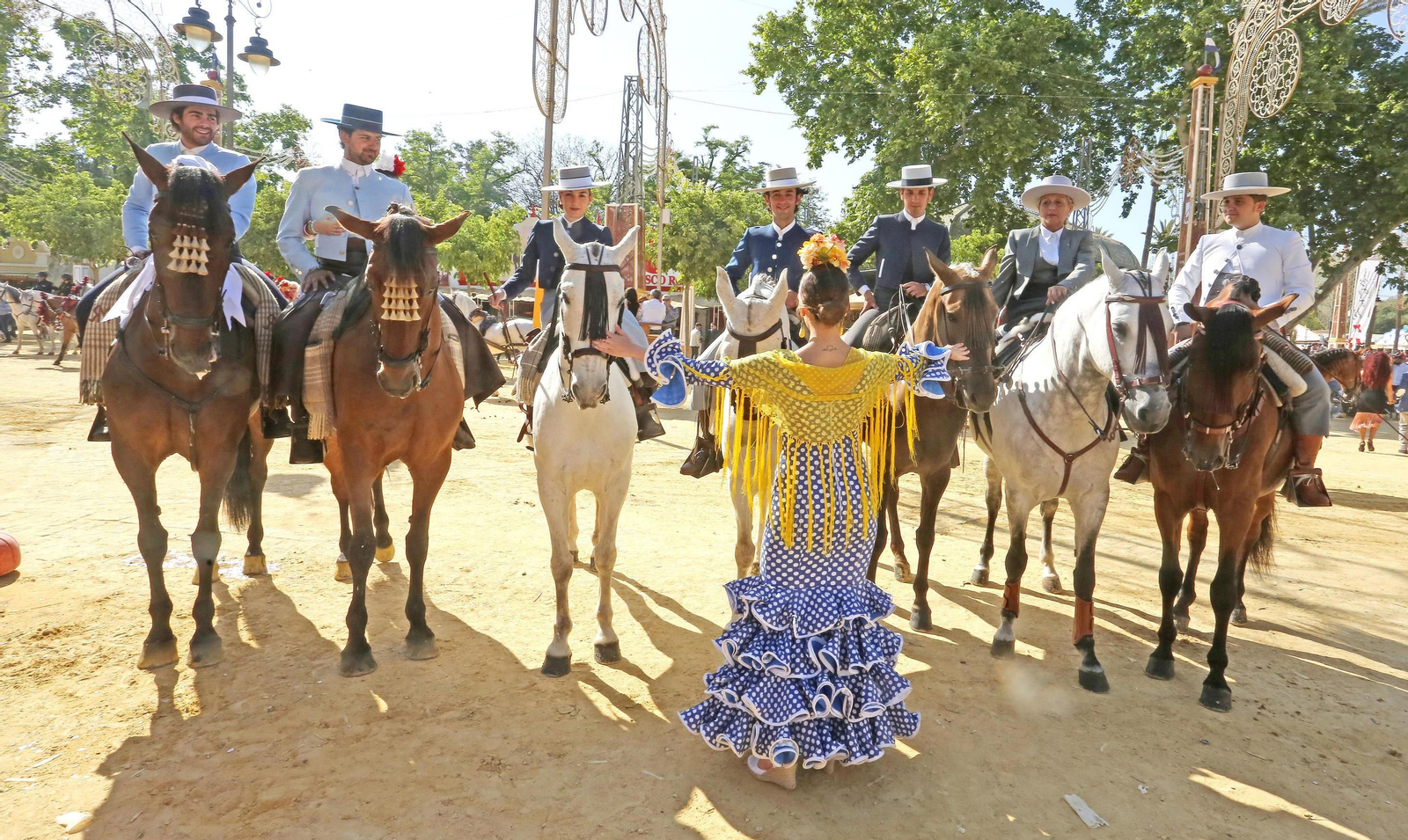 Una mujer vestida de flamenca ante siete jinetes en el Real del González Hontoria.