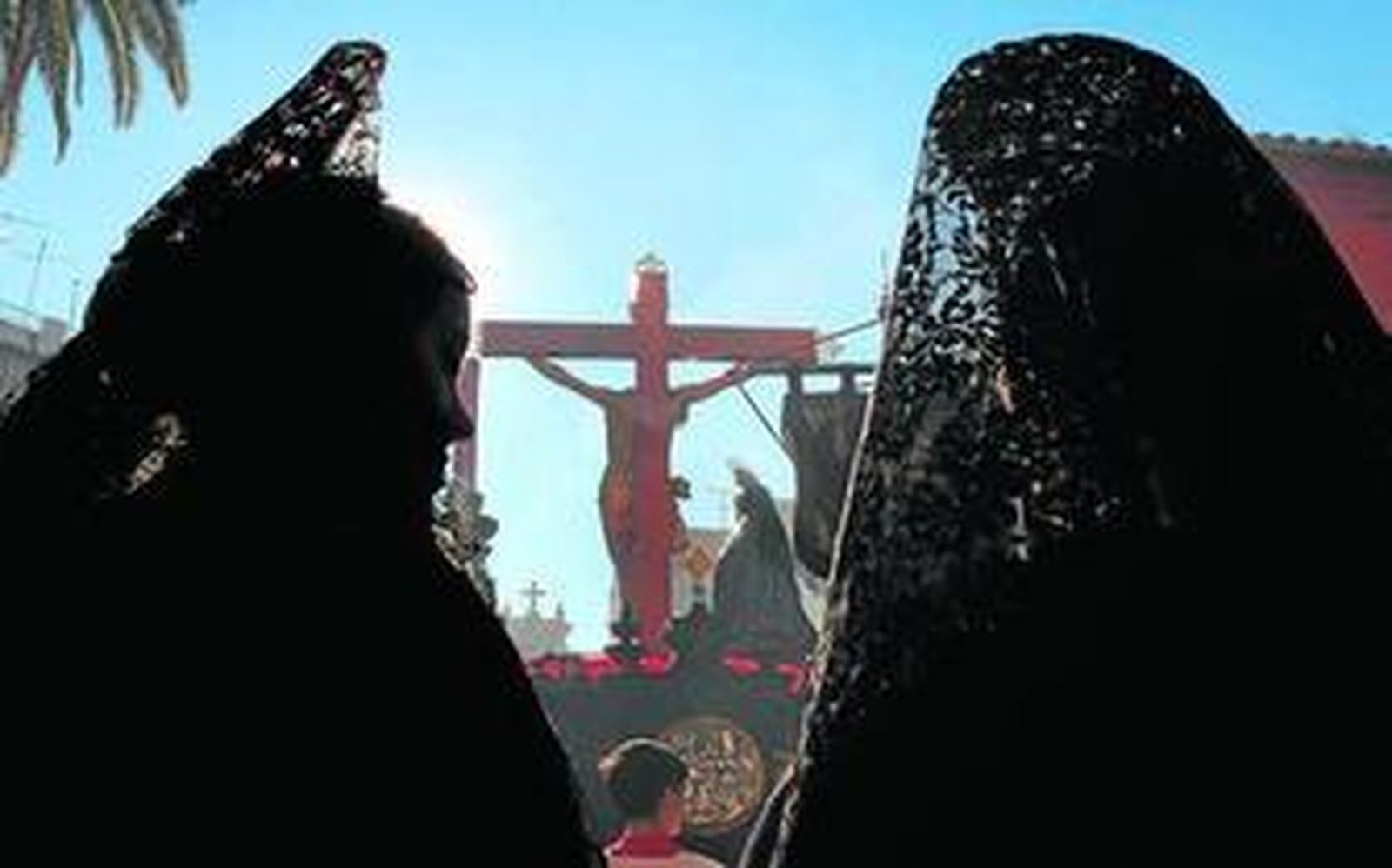 En Cristo de la Caridad, entre dos mujeres vestidas de mantilla y bajo un cielo sin nubes.