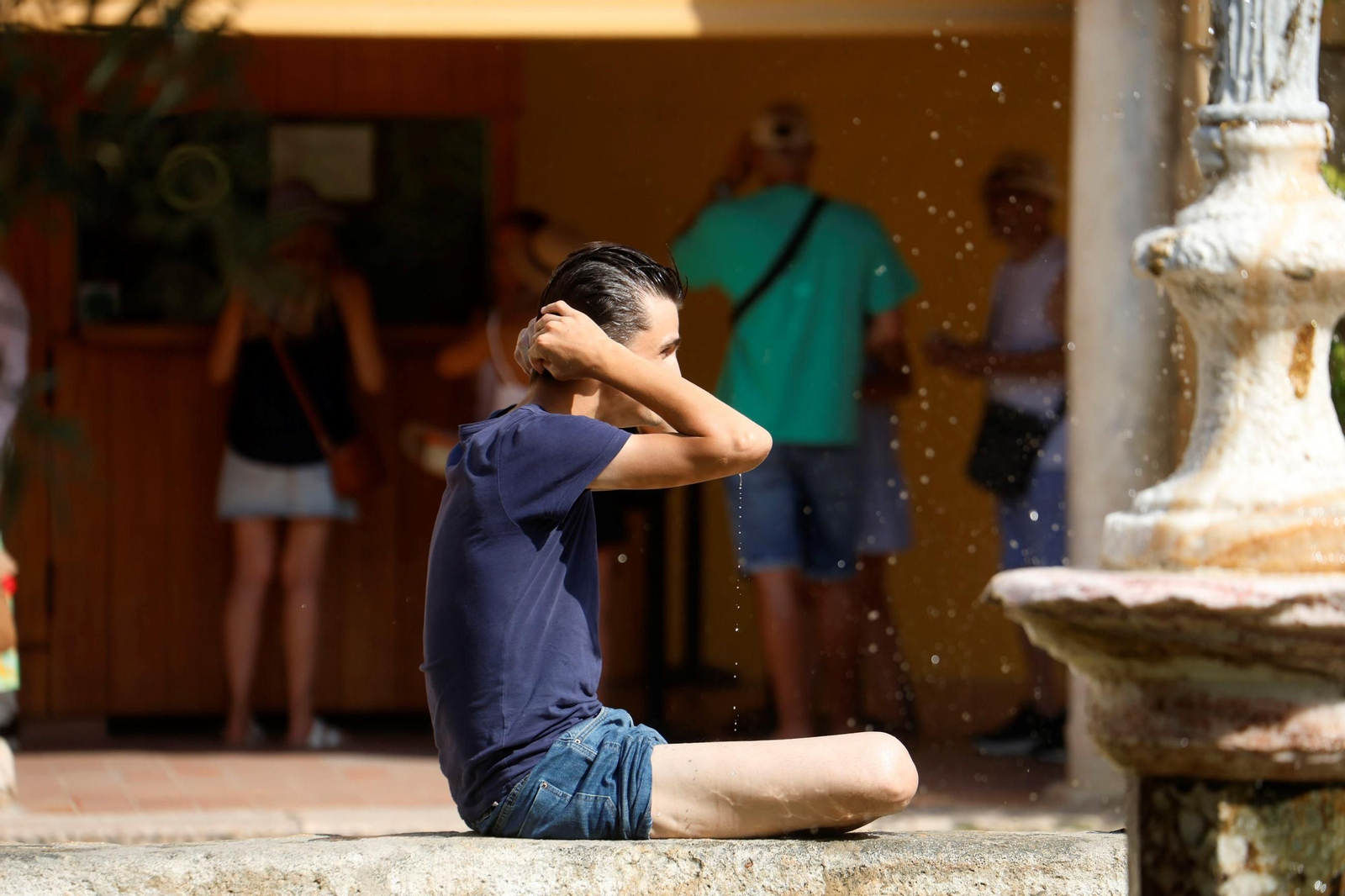 Un joven se refresca mojándose la cabeza en una de las fuentes del Patio de los Naranjos.