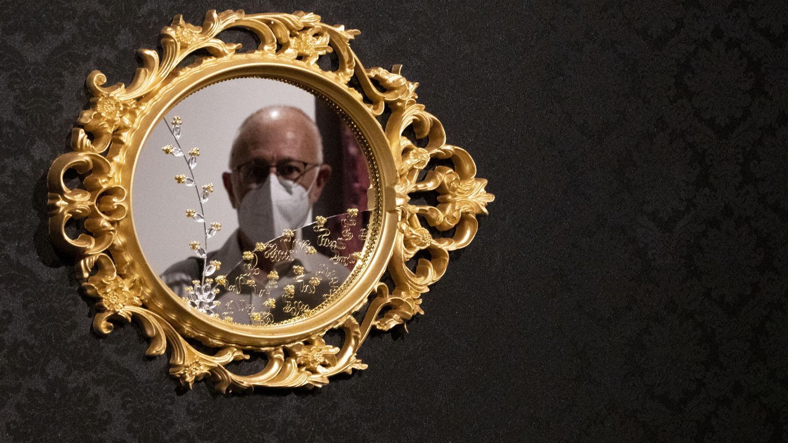 Un visitante reflejado en un espejo de la muestra