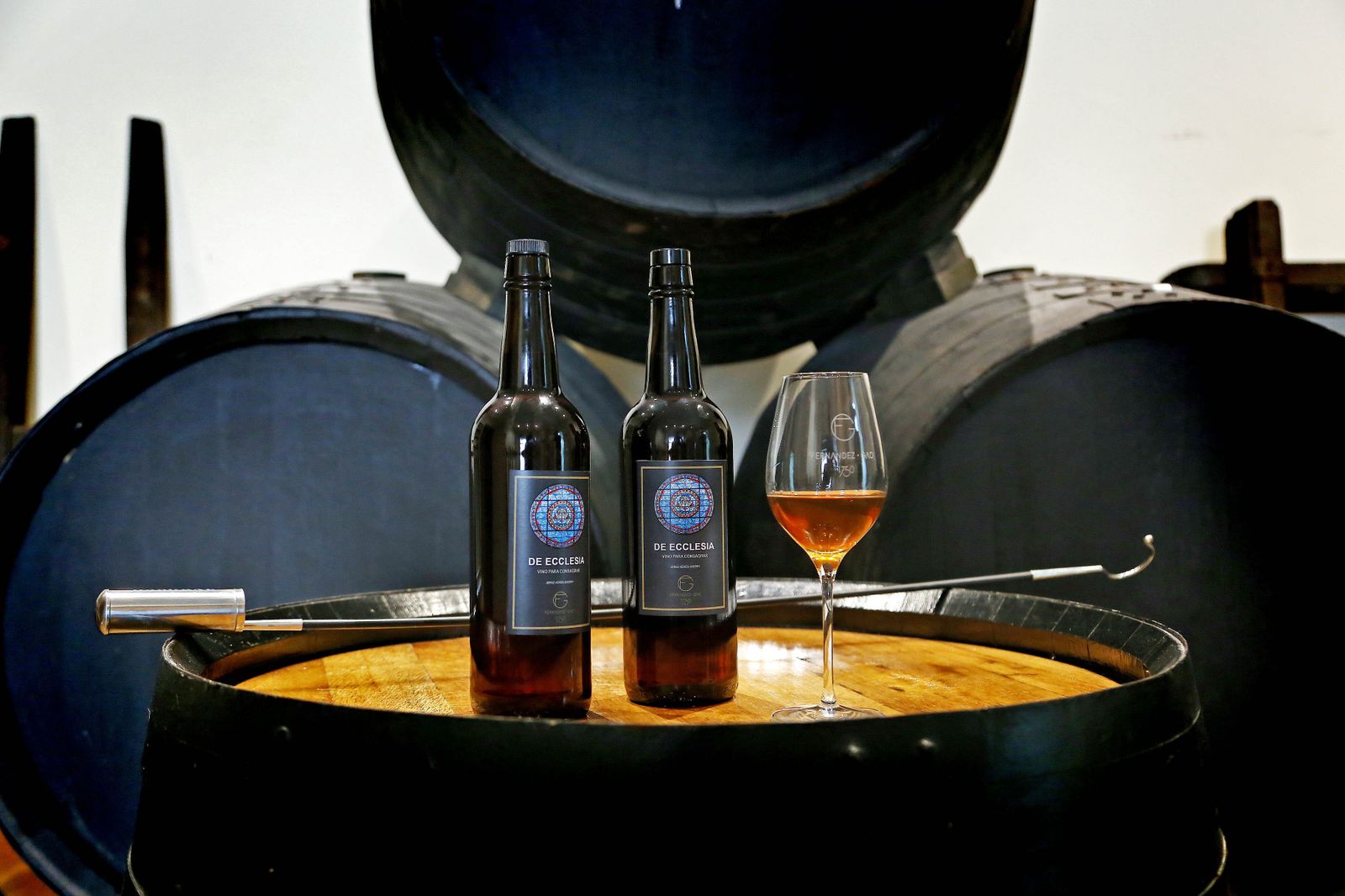 1. Dos botellas de la marca 'De Ecclesia',, la nueva gama de vinos de misa de la bodega jerezana Fernández-Gao junto a una copa de vino con el caldo servido. 2. Juan Carlos Sánchez Gago le muestra a Juan Antonio Vital la botella de su nueva gama de vinos de misa en la oficina del conjunto bodeguero 3. El director técnico de la bodega y el párroco de Algar posan con el vino de misa 'De Ecclesia'.