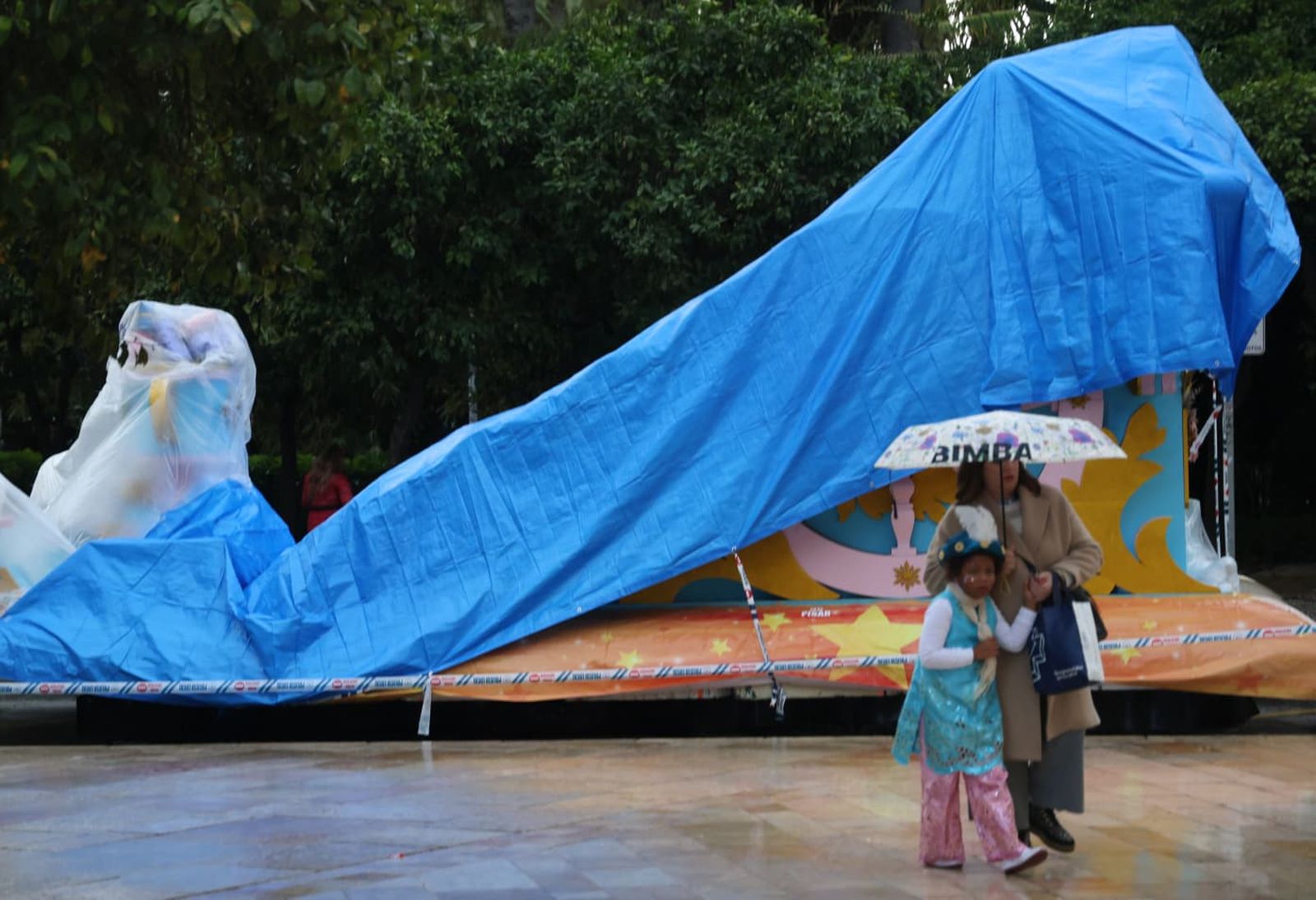 Una familia con paraguas pasa junto a una carroza cubierta en Málaga.