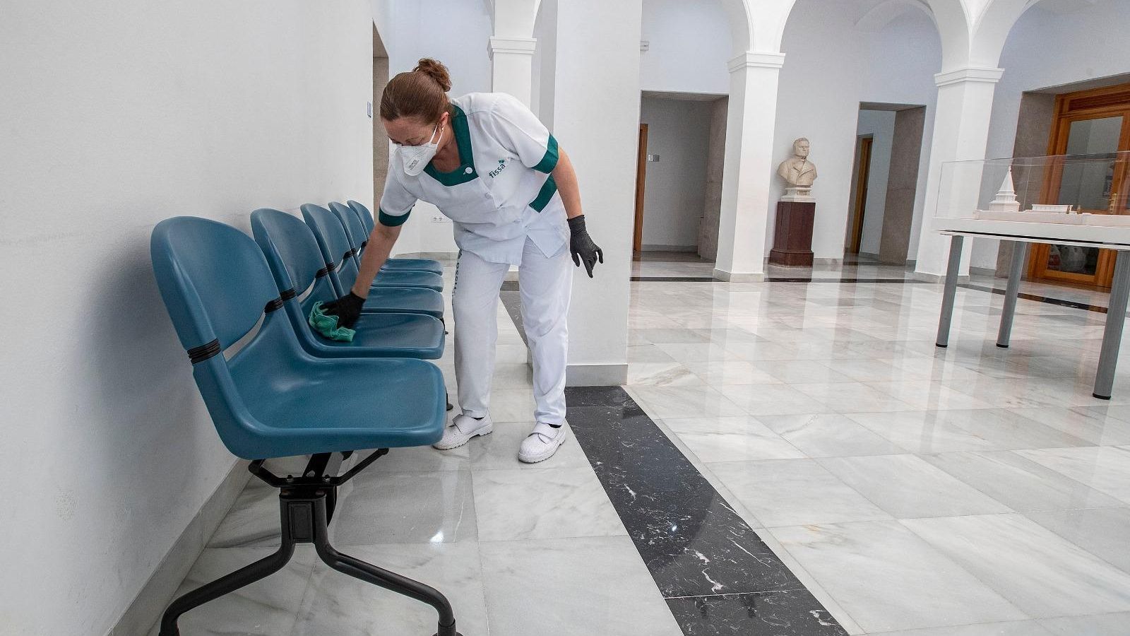 Una limpiadora desinfecta los asientos del patio interior de Alcaldía.