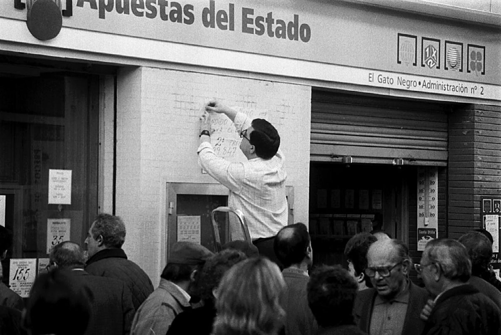 Un lotero coloca el cartel de un premio vendido en su administración.