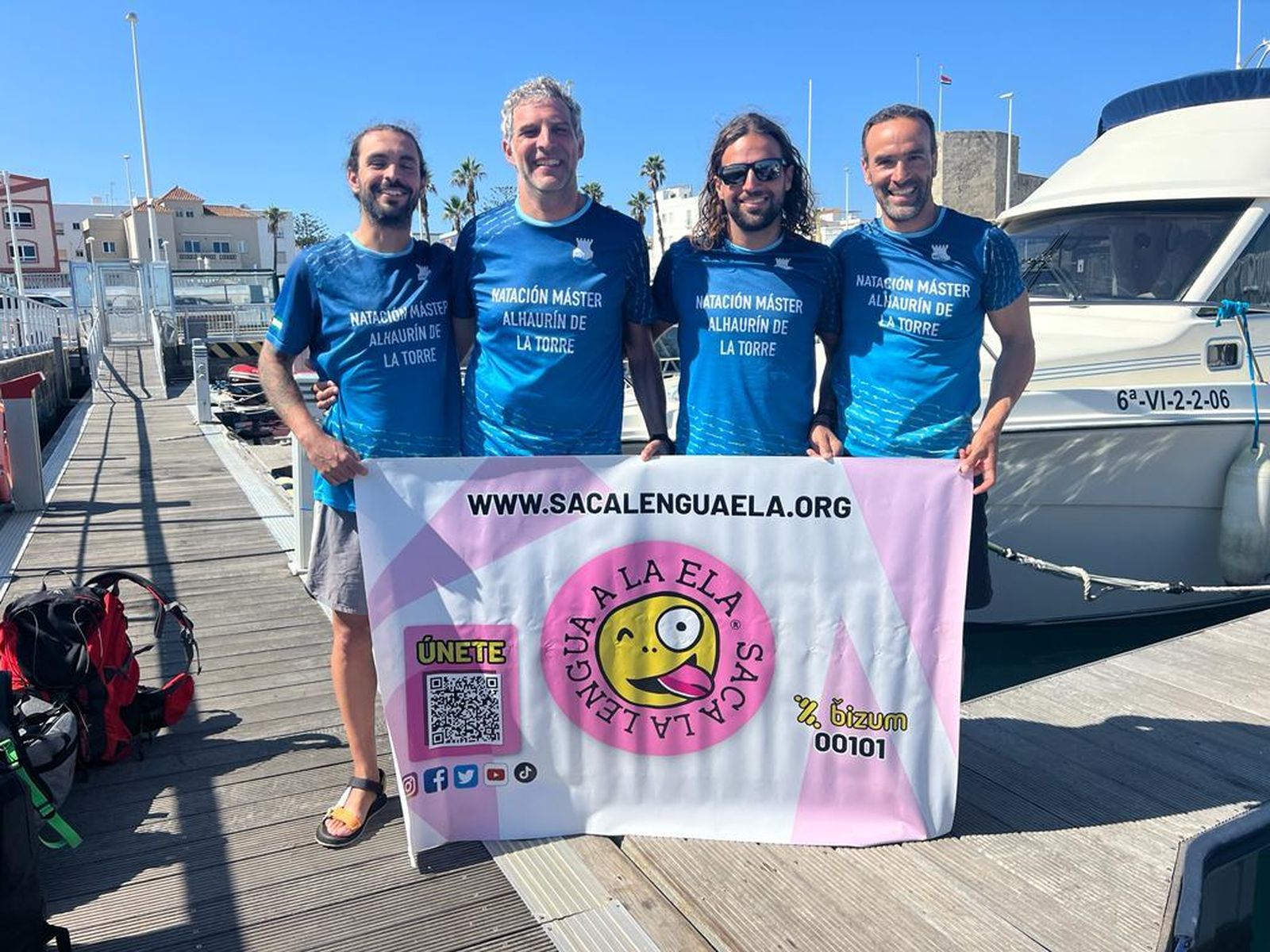 Los cuatro nadadores junto a la bandera que visibiliza el ELA