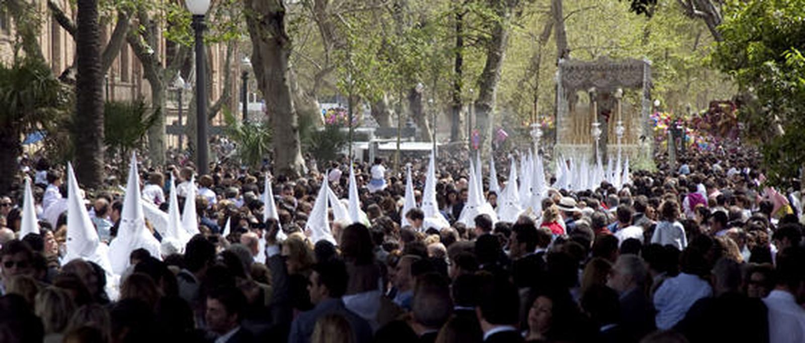 Imagen de la fila de nazarenos con la Virgen de la Paz de fondo a su paso por el Parque.

Foto: Jaime Martínez