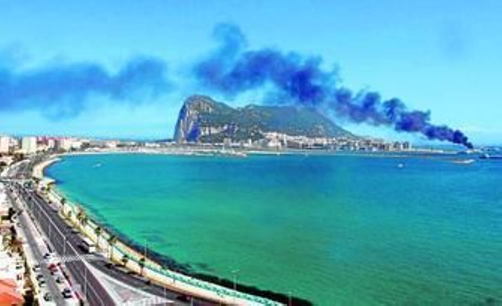 Imagen del peñón de Gibraltar y la columna de humo que emerge desde las instalaciones portuarias, ayer por la tarde, en una imagen tomada desde la avenida España de La Línea.