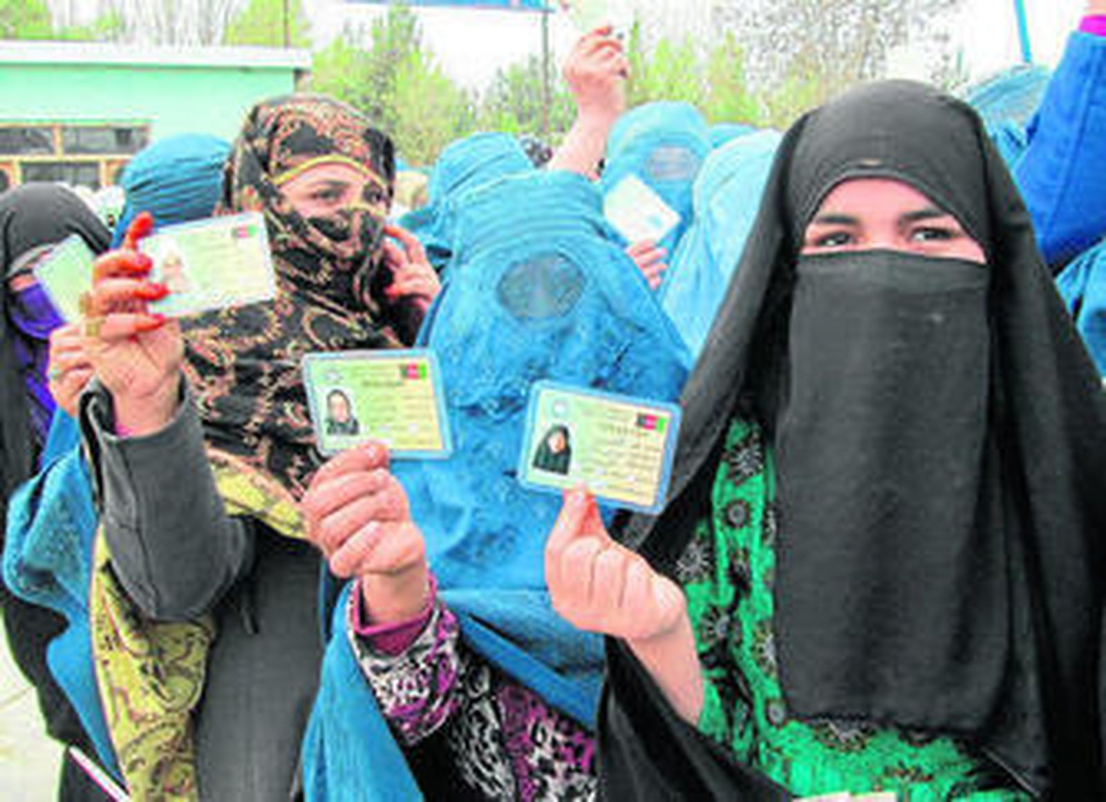 Varias mujeres con 'burka' enseñan sus carnés para votar mientras esperan su turno en Kunduz.