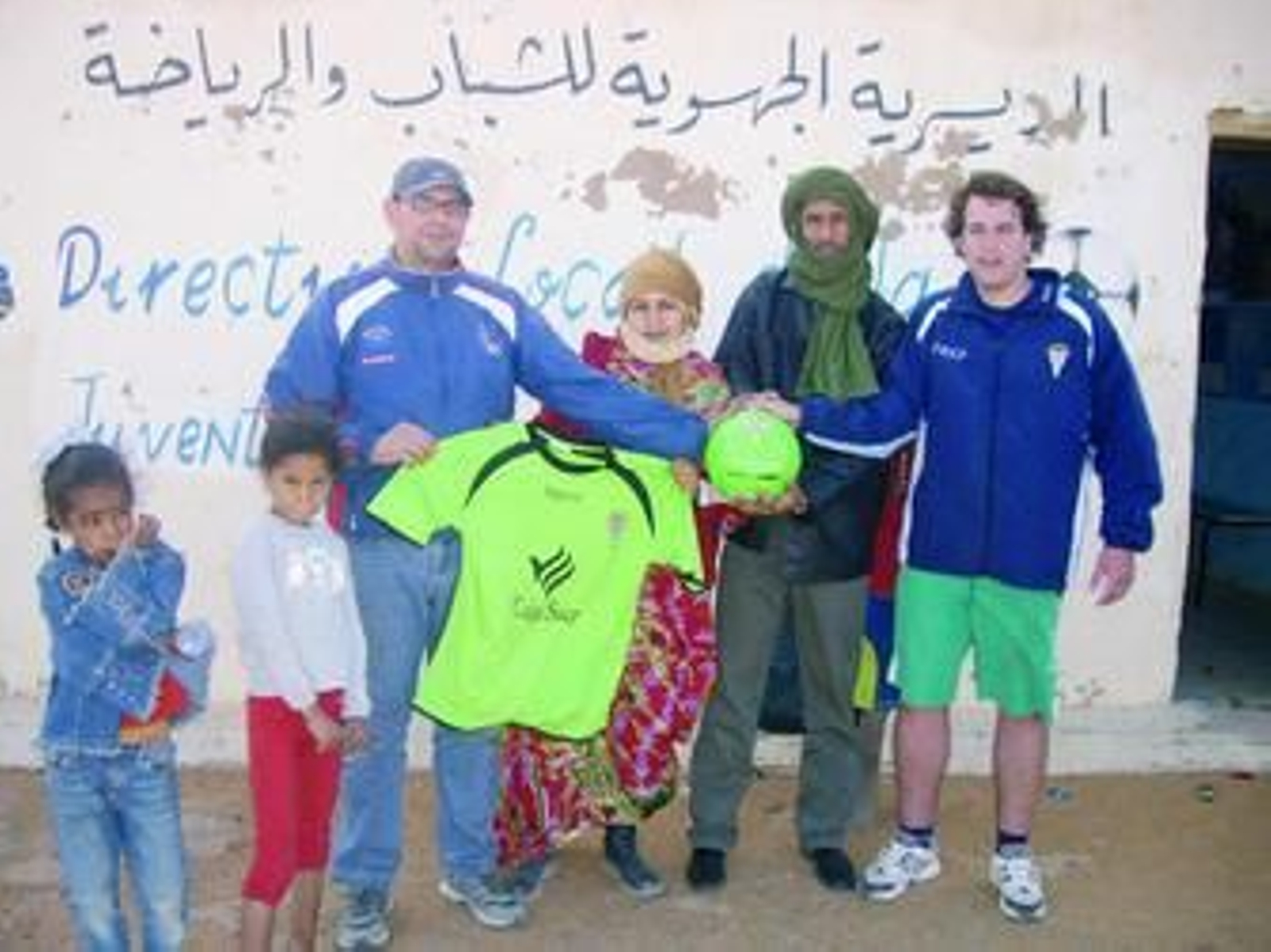 1. Elías Cabrera, el primero por la derecha, posa con un grupo de saharauis. Entre todos sostienen un balón y una camiseta del Córdoba, que ha enviado material deportivo para enriquecer las escuelas de la zona. 2. Un niño, ataviado con la equipación blanquiverde, corre detrás de un balón en el campamento destinado a los refugiados.