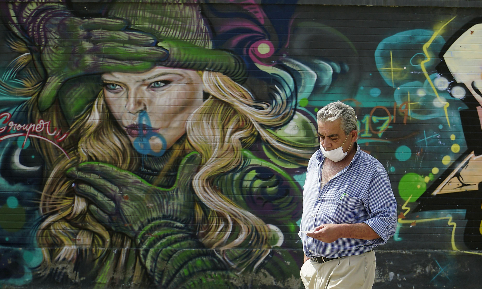 Un viandante camina junto a uno de los grafitis de Tres Barrios-Amate.