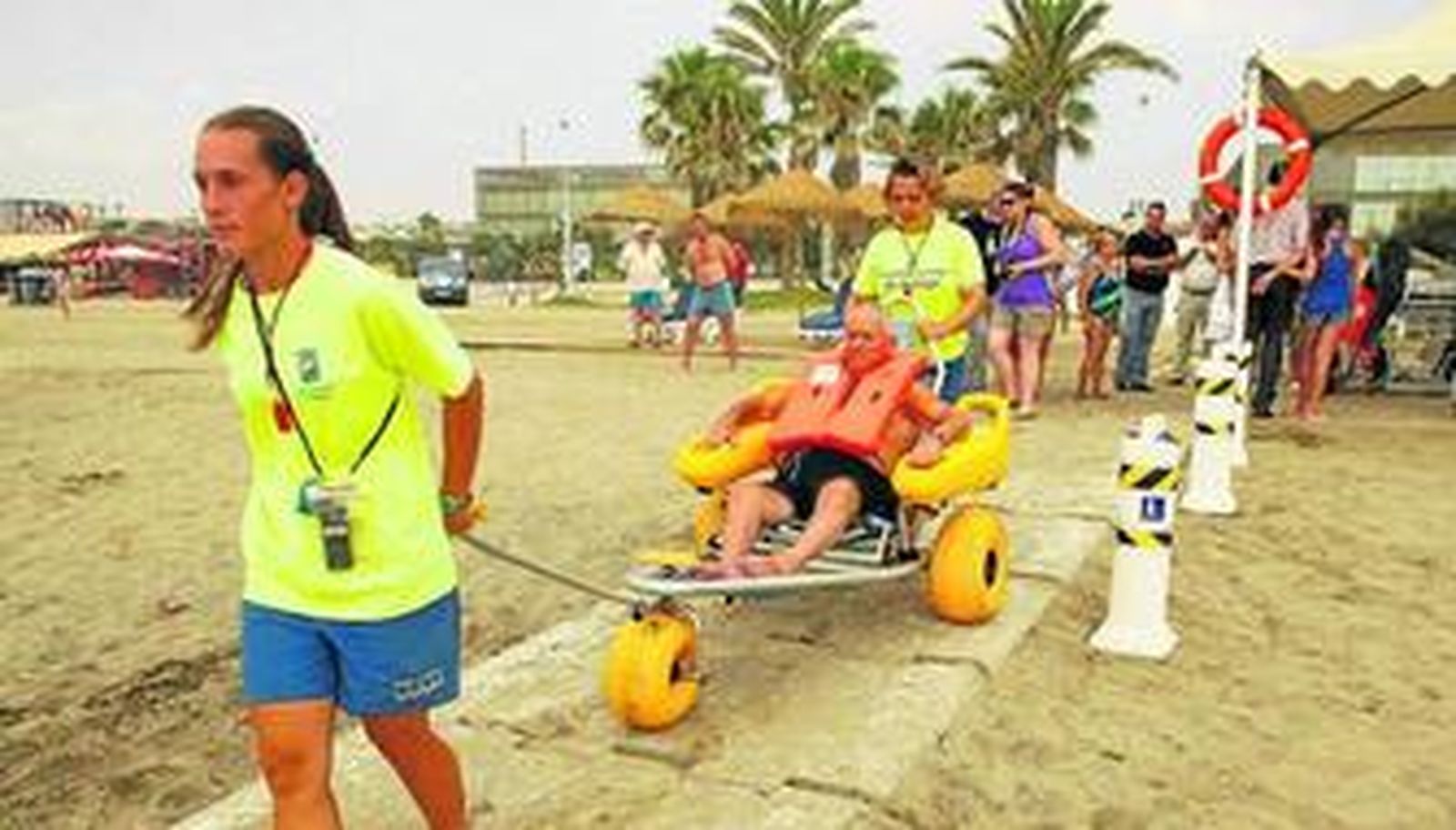Dos socorristas, ayer, mientras transportan a un bañista en una silla anfibia al interior del agua en la playa de La Misericordia.