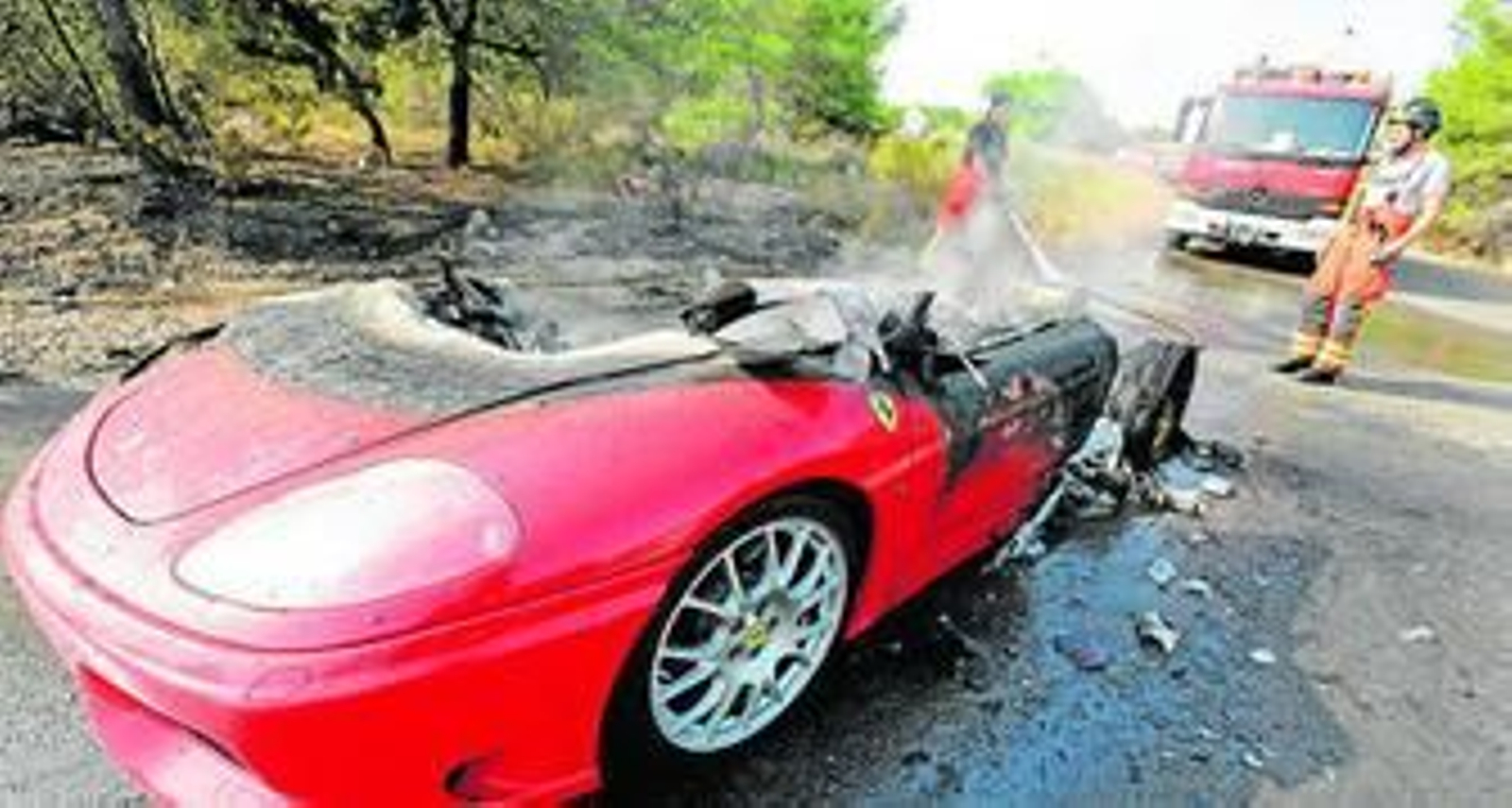 Un par de bomberos enfría los restos del Ferrari de Banega tras el incendio sufrido.