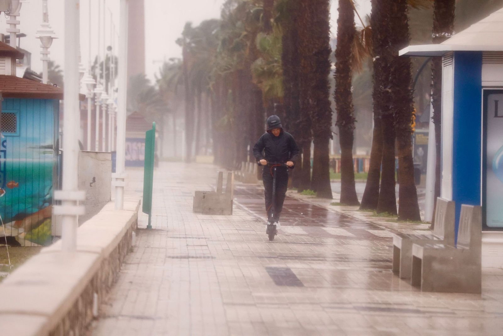 Un joven circula en patinete bajo un fuerte chaparrón en Málaga.