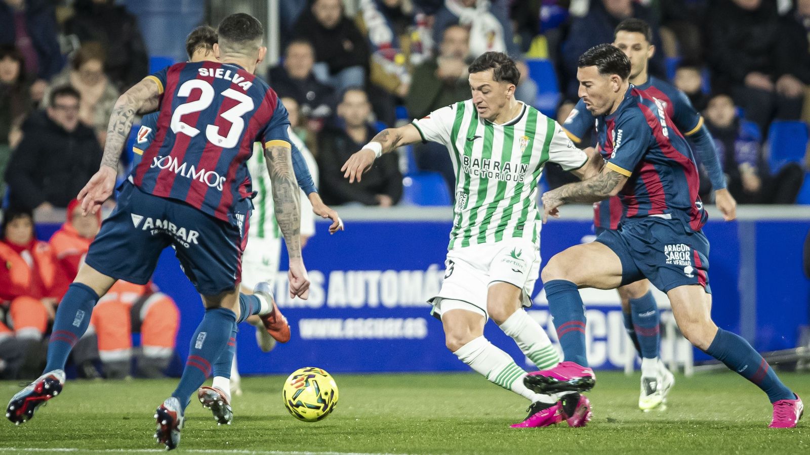 Carracedo conduce el balón entre varios rivales en el Huesca - Córdoba CF.