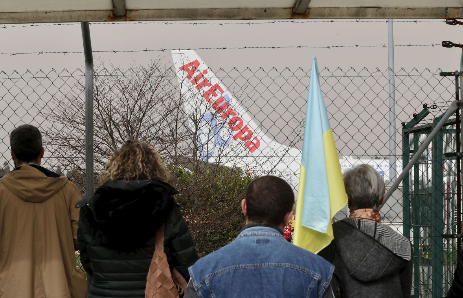 Varias personas con banderas de Ucrania esperan la llegada de un avión al aeropuerto.