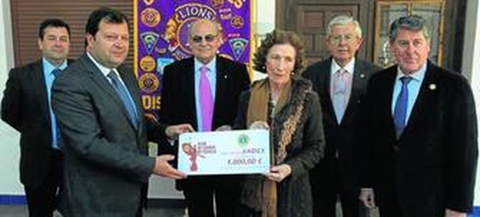 Aurelio León Andújar y María Luisa Guardiola muestran el cheque de 'Navidades para Andex' junto a Miguel Gallego, a la derecha, y otros asistentes en segundo plano.