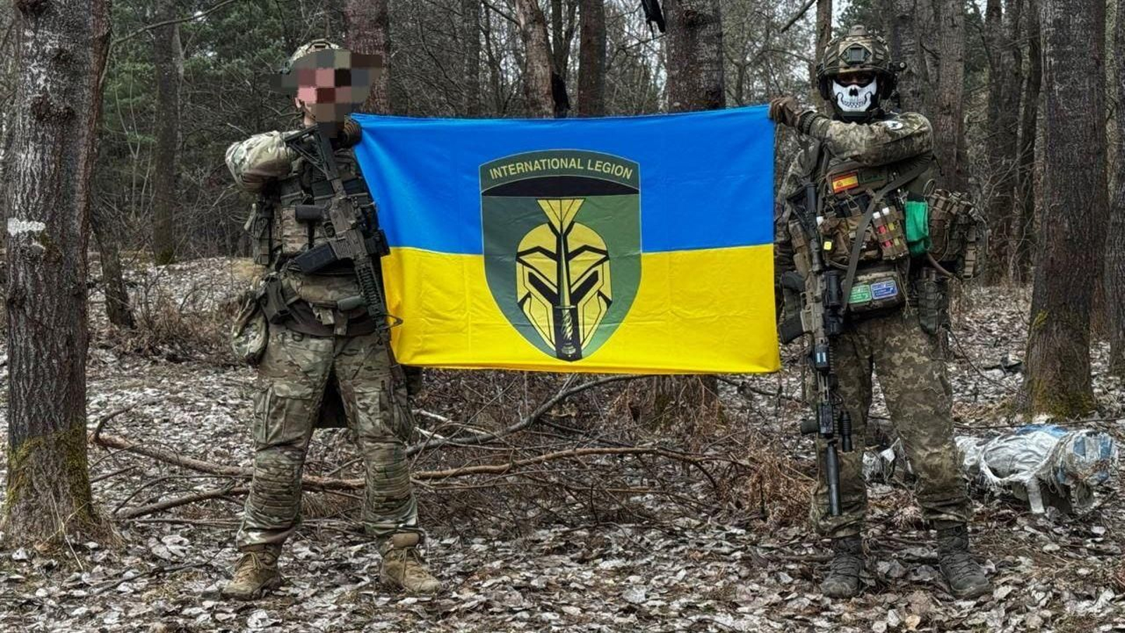 Ren -derecha- soldado algecireño, posa junto a un compañero en un lugar del frente de batalla con la bandera de Ucrania, con el logotipo de la Legión Internacional.