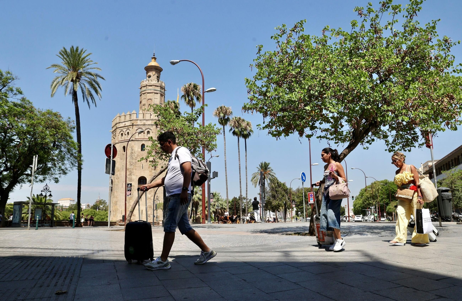 Varios turistas arrastran sus maletas por delante de la Torre del Oro.