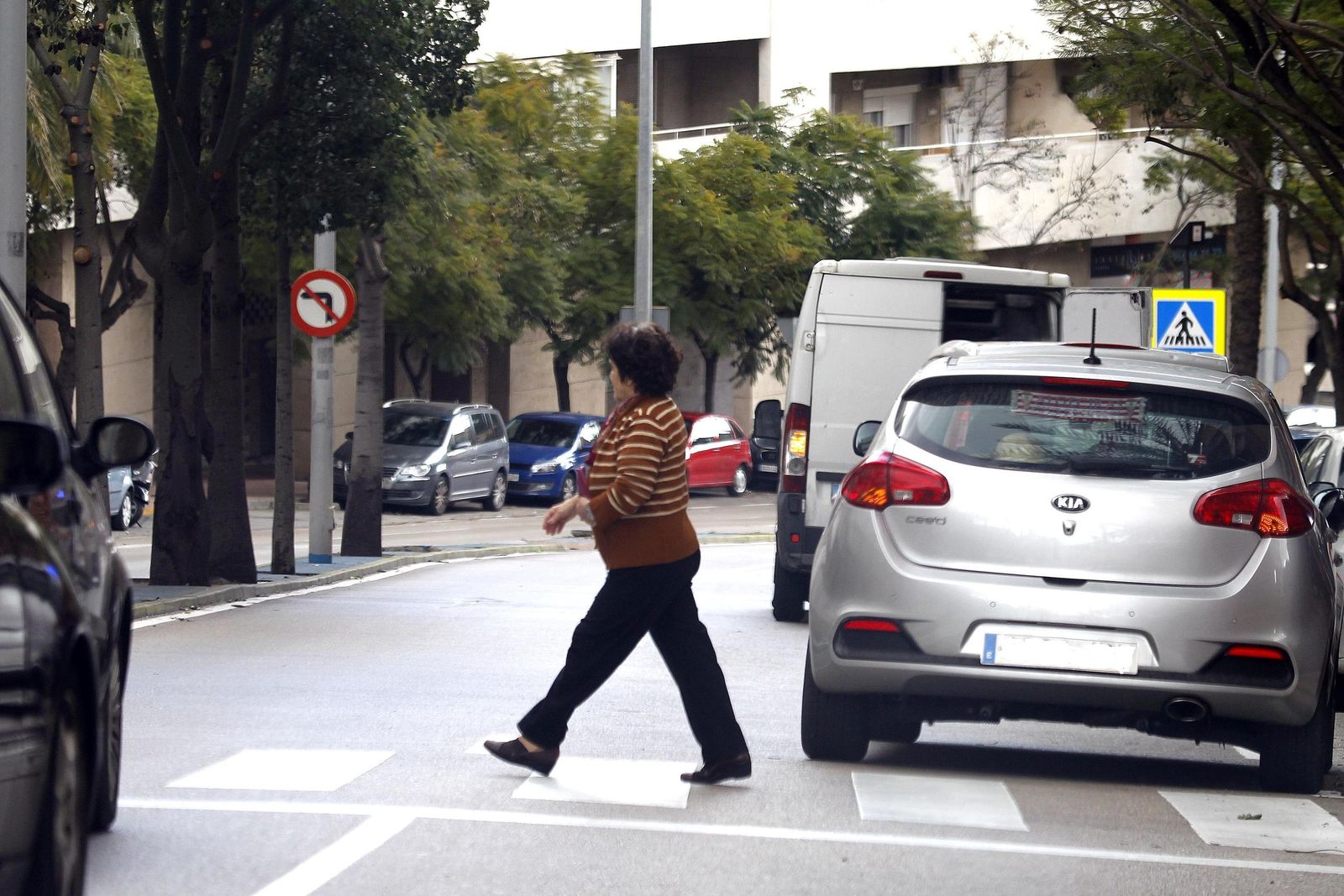 Una mujer pasa junto a un coche parad en doble fila.